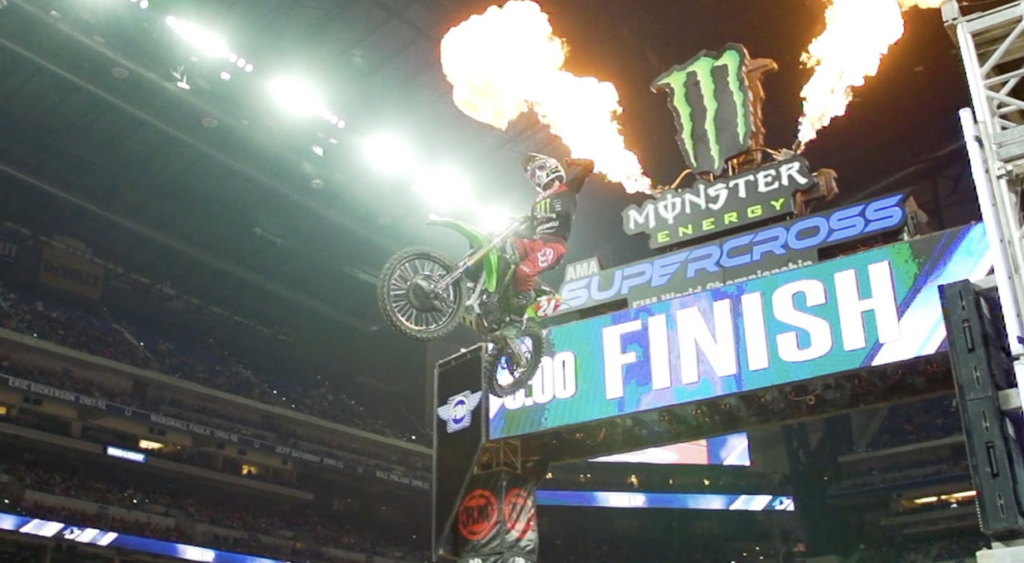 Image of Feld Entertainment's Supercross Event with a motorcycle driver, flying through flames in the air.